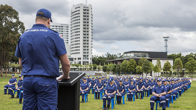 A student representing the first class of Paramedic Trainees to join NSW Ambulance under the new Post Employment Tertiary Pathway stands on a podium at Sydney's Olympic Park to address his fellow students.