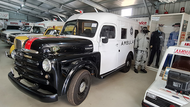 A row of historic ambulance vehicles and ambulance uniforms on display inside the Temora Ambulance Museum.