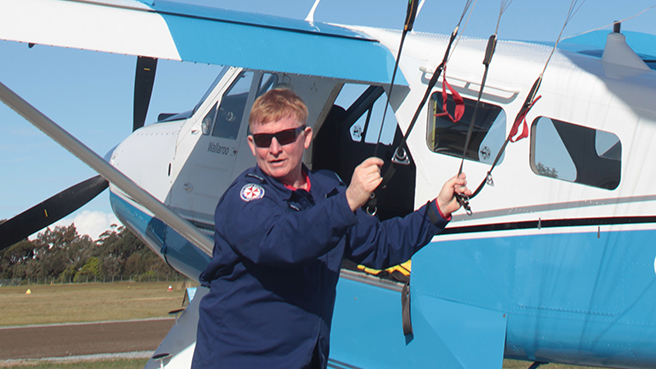Trainee Paramedic and veteran skydiver Rob McMillan holding his chute next to a light plane